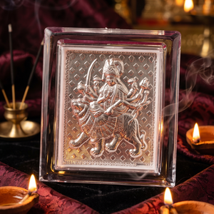 Silver deity panel in a glass frame with candles and incense on a dark background