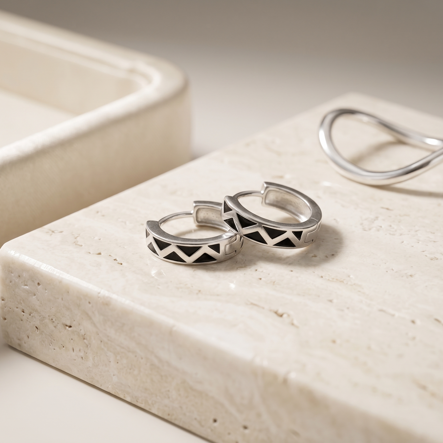 Silver hoop earrings on a textured beige surface with a neutral background