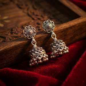 Ornate silver earrings on a wooden surface with a red fabric background
