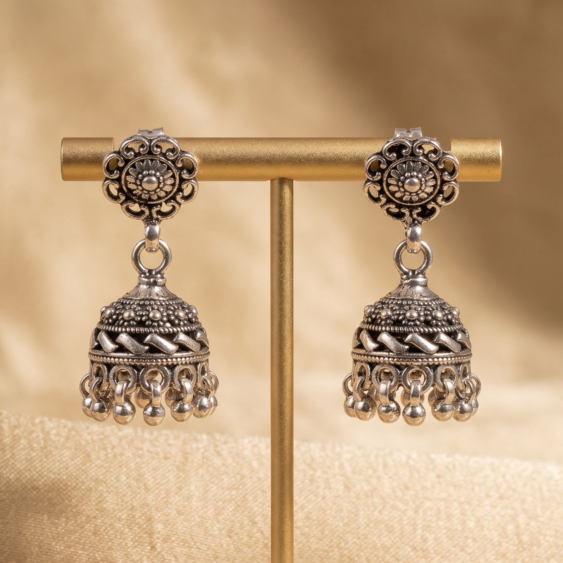 Pair of silver earrings on a gold stand with a beige background