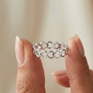 Silver ring with heart designs held between two fingers against a neutral background