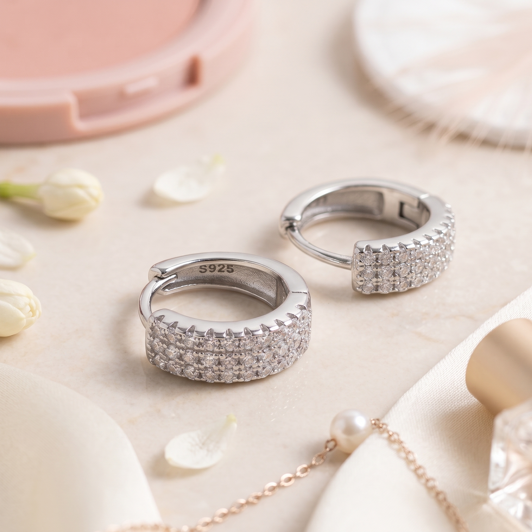 Two silver rings on a light surface with flowers and a perfume bottle.