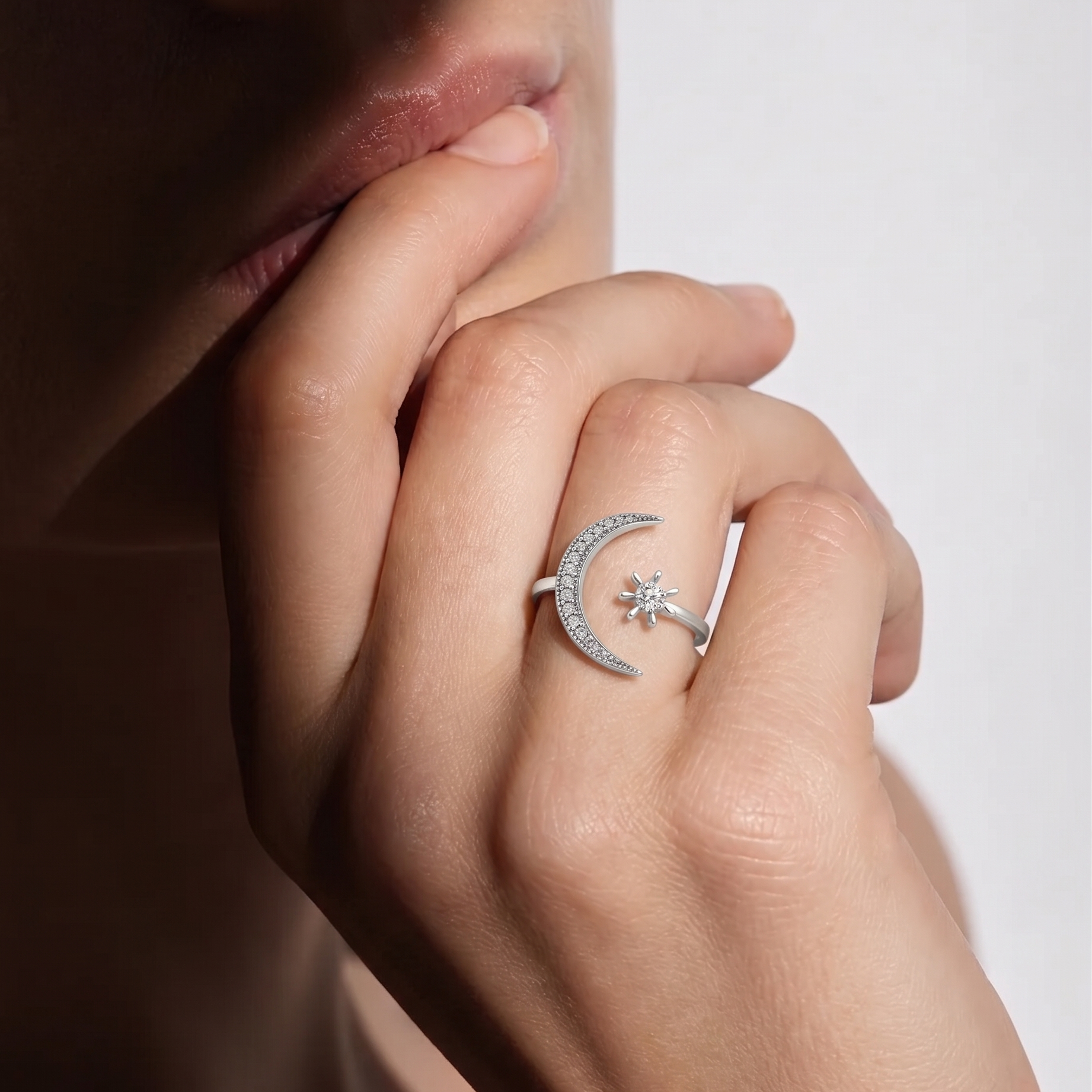 Close-up of a hand wearing a silver ring with a moon and star design on a neutral background