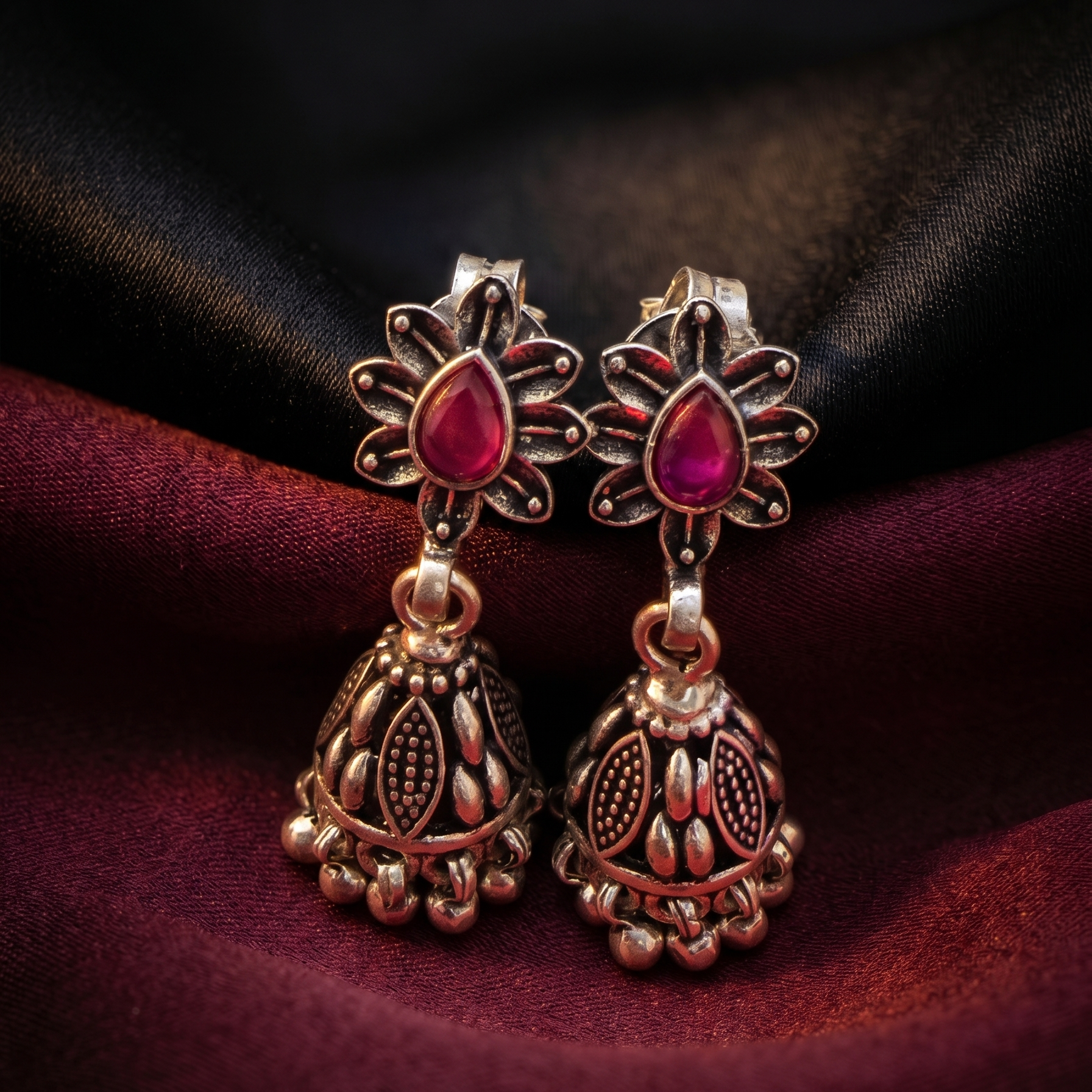 Ornate earrings with red gemstones on a dark fabric background