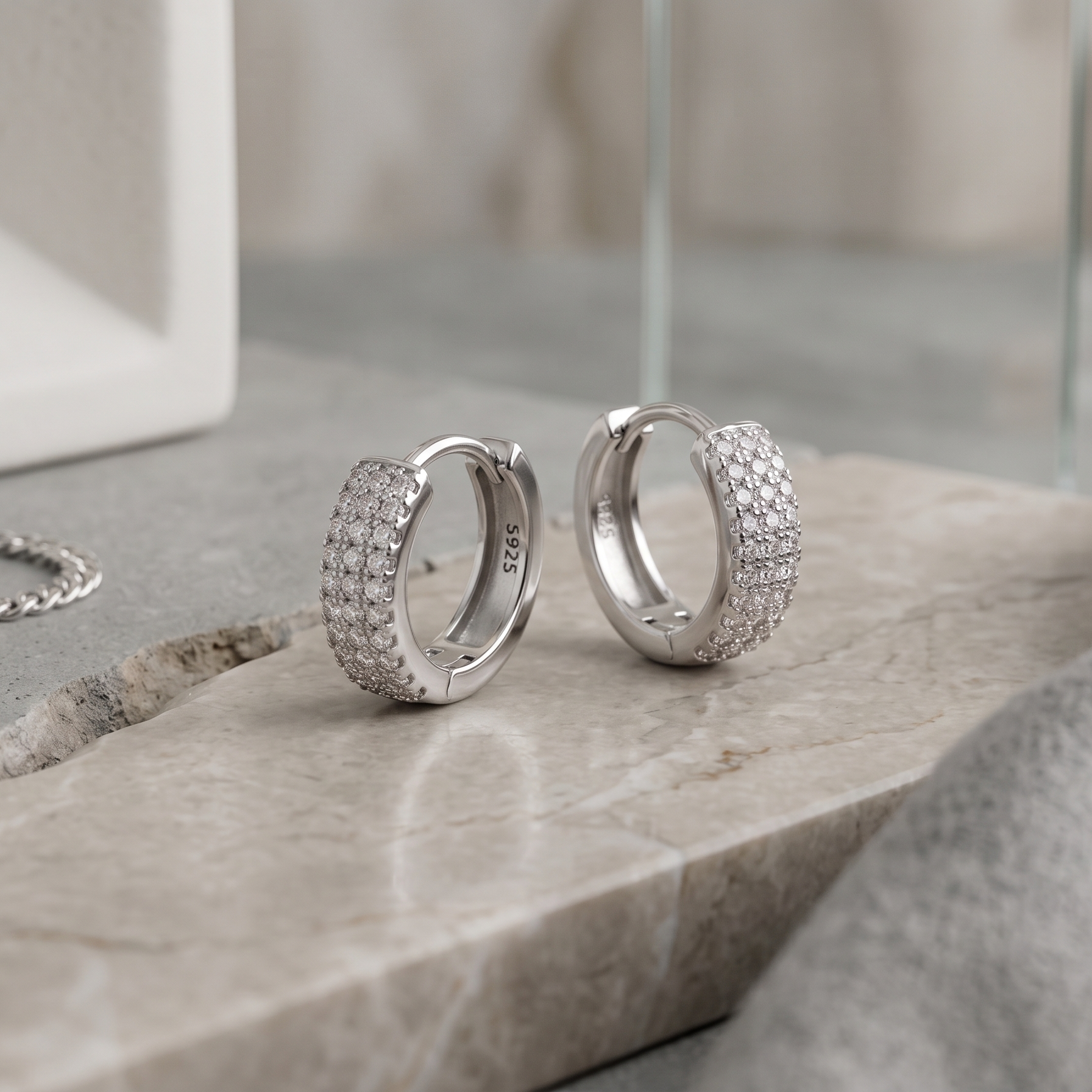 Silver hoop earrings with embedded stones on a stone surface