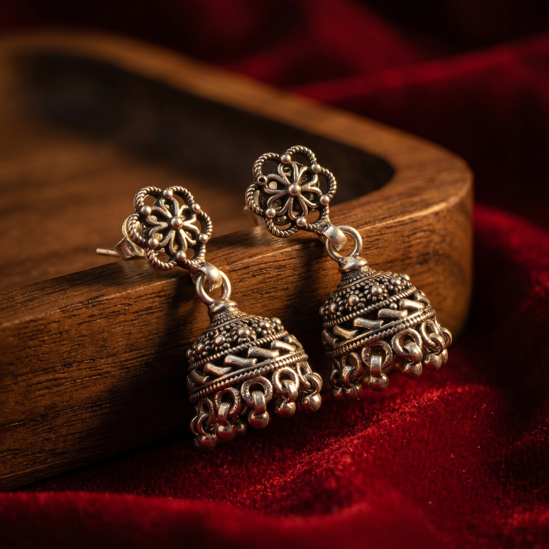 Ornate silver earrings on a wooden stand with a red fabric background