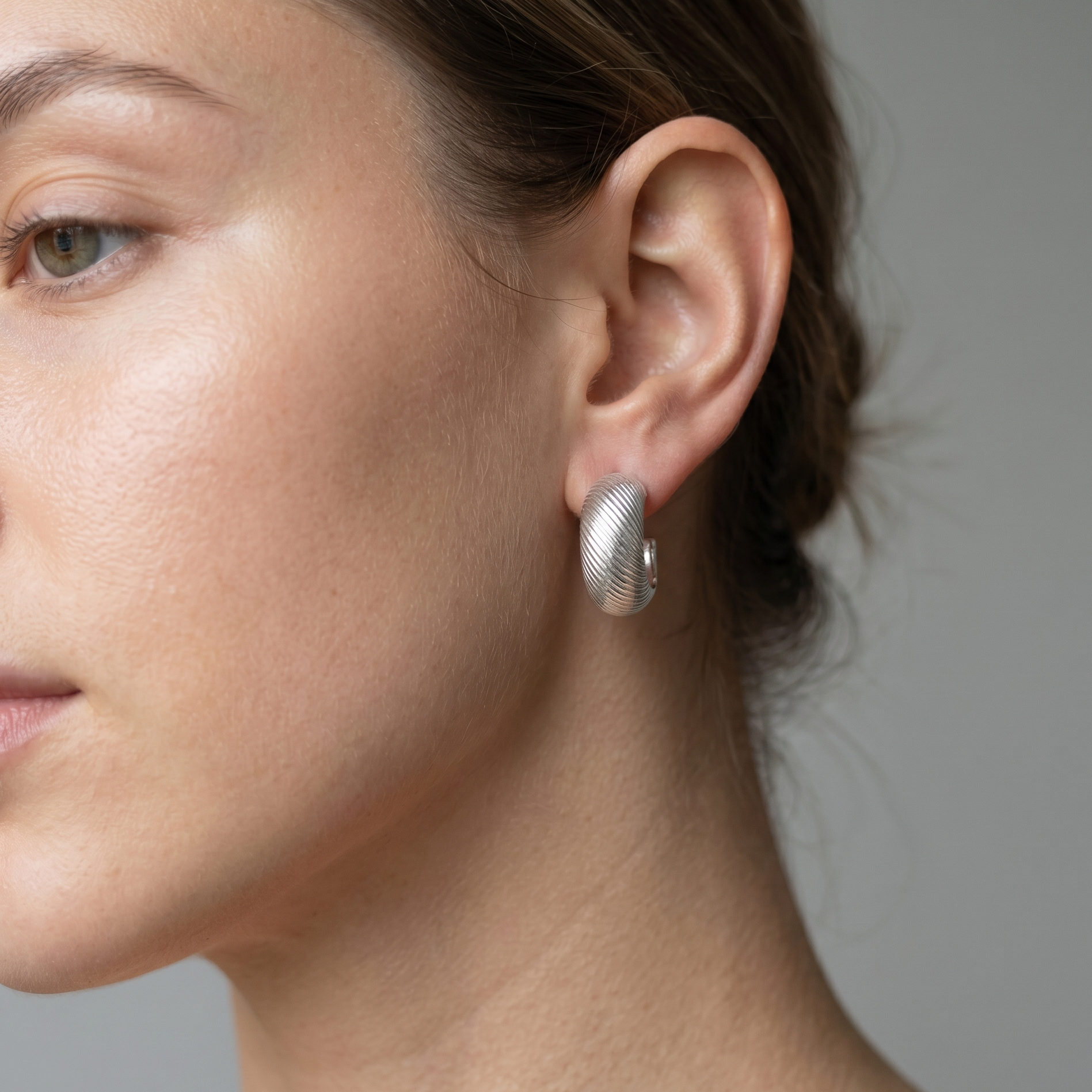 Close-up of a woman wearing silver earrings against a neutral background