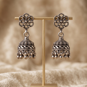 Ornate silver earrings on a 'lustra' stand with a beige background