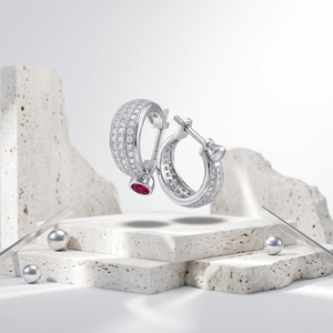 Silver hoop earrings with a red gemstone on a stone-like surface with a white background
