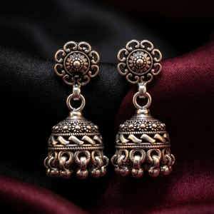 Pair of ornate silver earrings on a dark fabric background